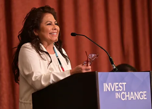 Woman speaking at a podium with signage on the front that reads: Invest in Change