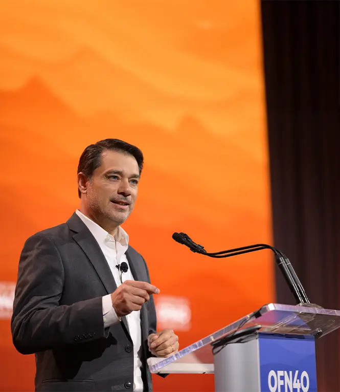 The CEO of PeopleFund speaks onstage at a podium in front of an orange backdrop.