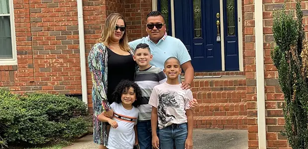 Family of 5 posing for group photo outside of brick home.