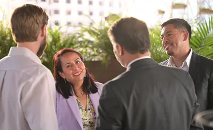 Four people in suits stand outside at a reception, engaged in conversation.