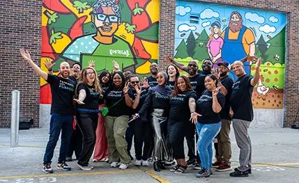 Members of the ProsperUs team pose for a photo outdoors in front of a colorful mural.
